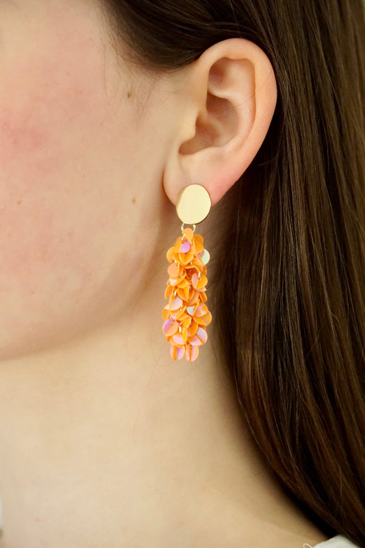 Ohr mit orangenem Ohrring mit Paliettentroddel